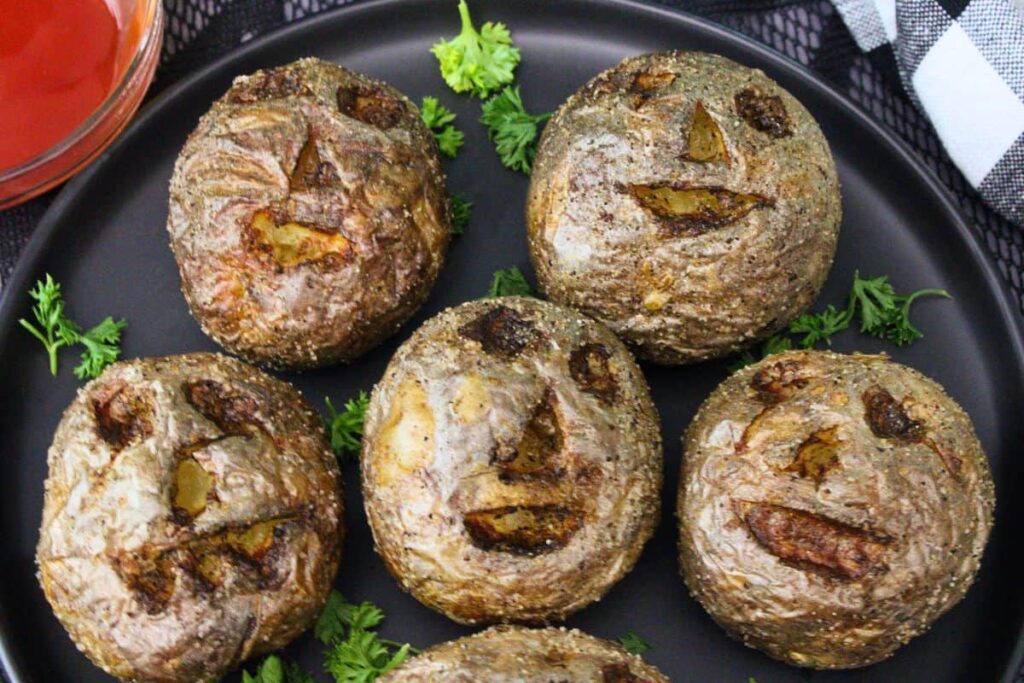 five air fryer halloween potatoes on a black plate showing off various spooky faces