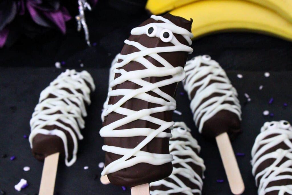 holding up a banana mummy showing off the dark and white chocolate strips and googly candy eyes