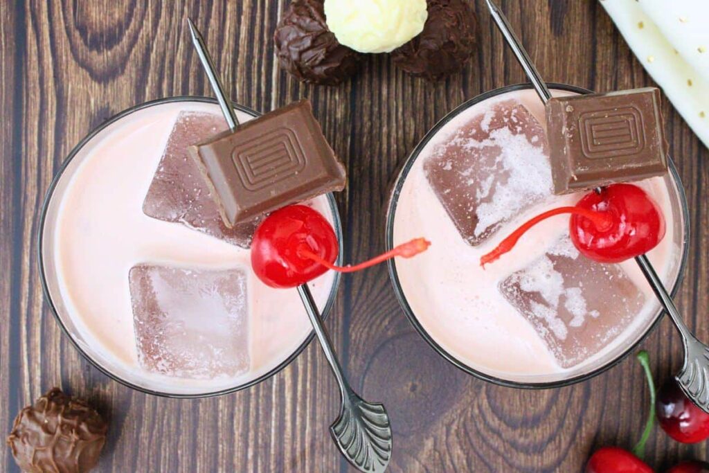 overhead view of two black forest cake cocktails with a maraschino cherry and ice on a wooden table