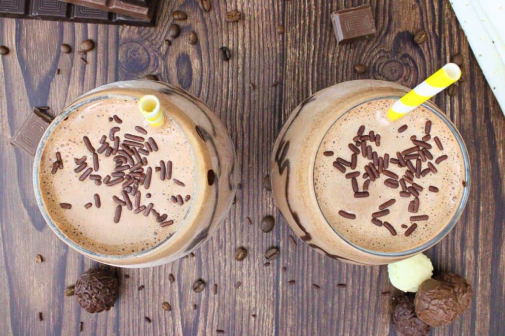 overhead view of two chocolate mudslides with chocolate sprinkles and striped straw on a wooden table