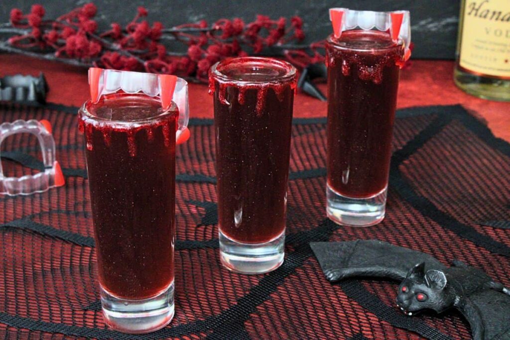 three vampire bite shots in a row with fake vampire fangs and spider web cloth background