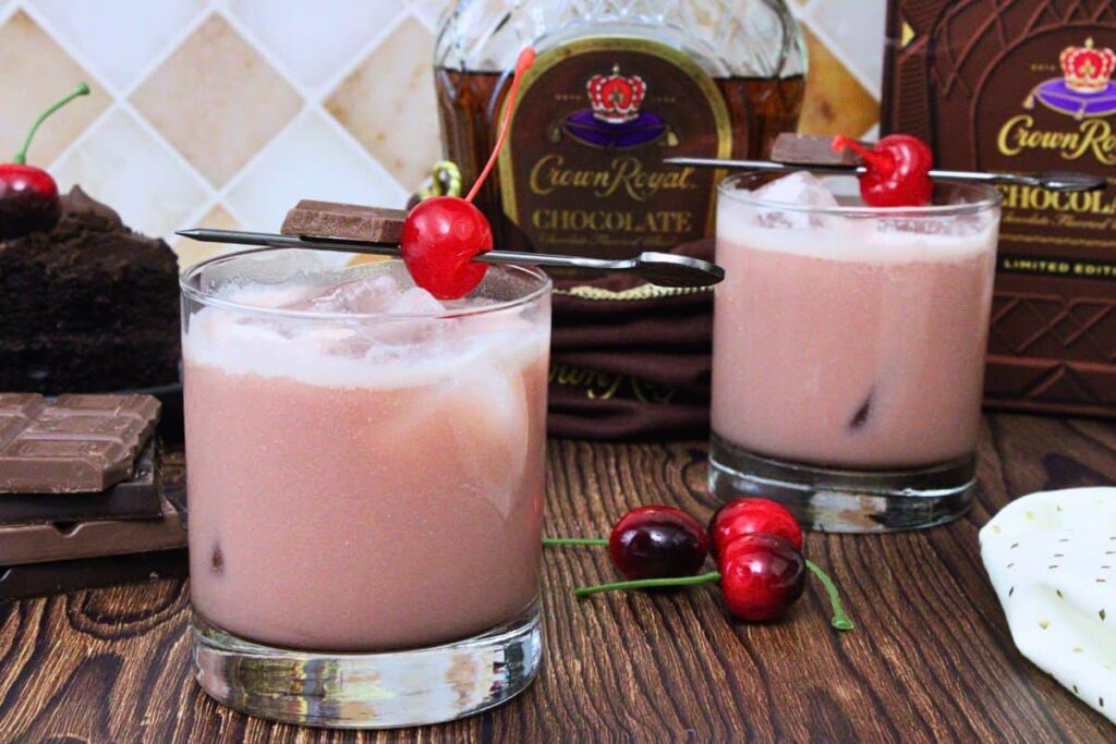 two black forest cake cocktails garnished with maraschino cherry in front of crown royal chocolate bottle