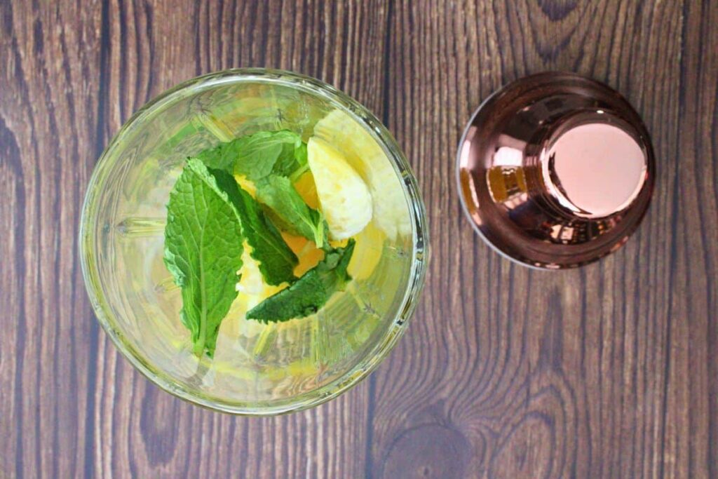add orange wedges, mint leaves, and orange juice to cocktail shaker