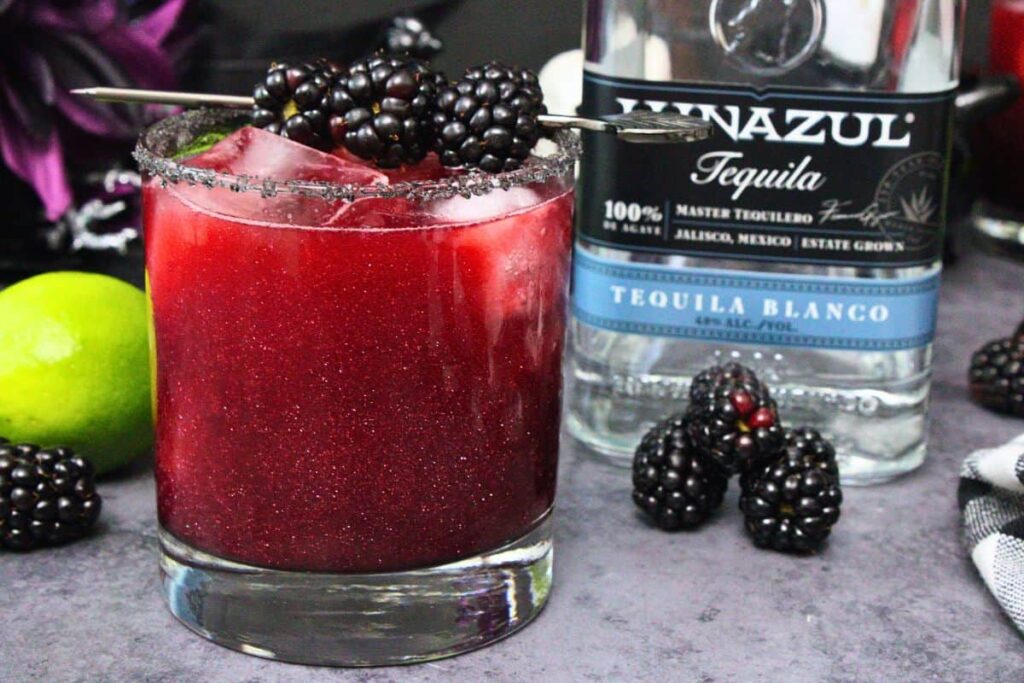 black magic margarita with blackberry skewer next to tequila bottle