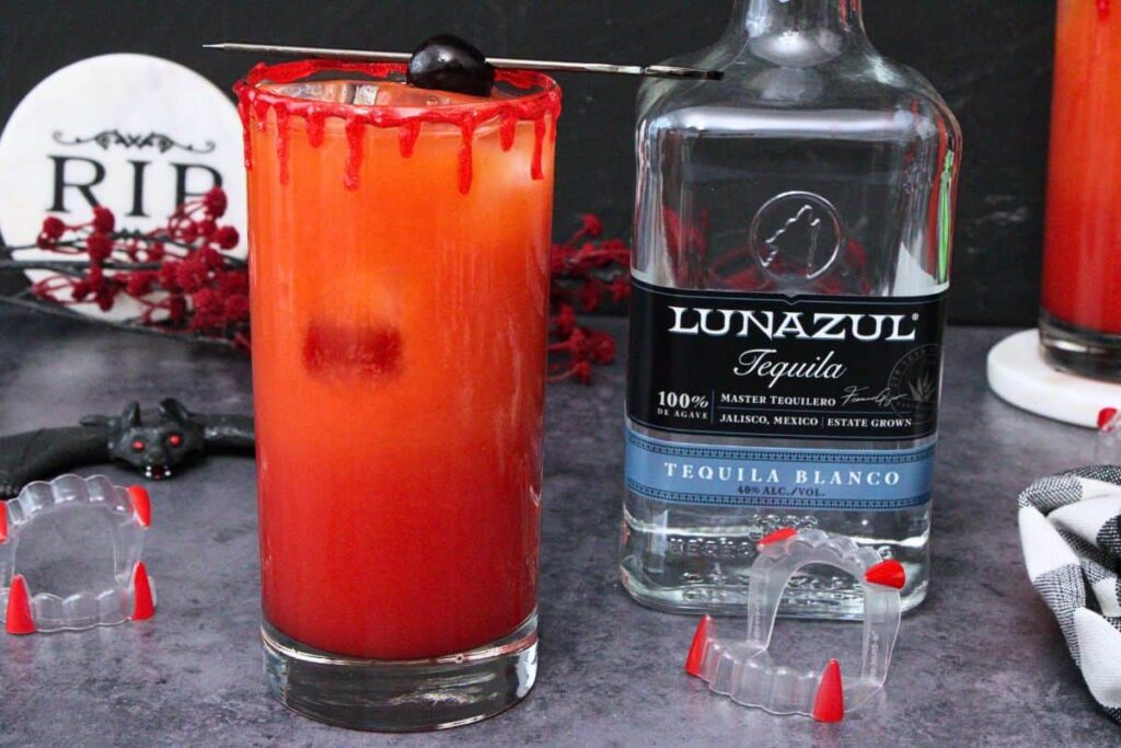 bloody vampire tequila sunrise next to tequila bottle surrounded by vampire fangs