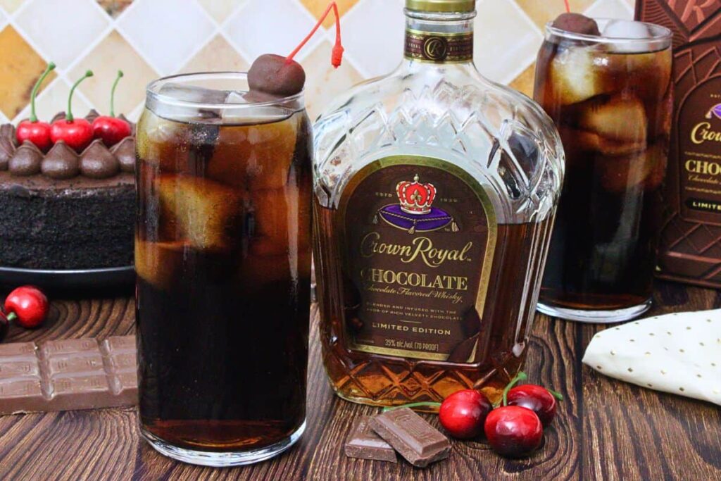 crown chocolate and cherry coke next to a chocolate crown royal bottle surrounded by chocolate and cherries