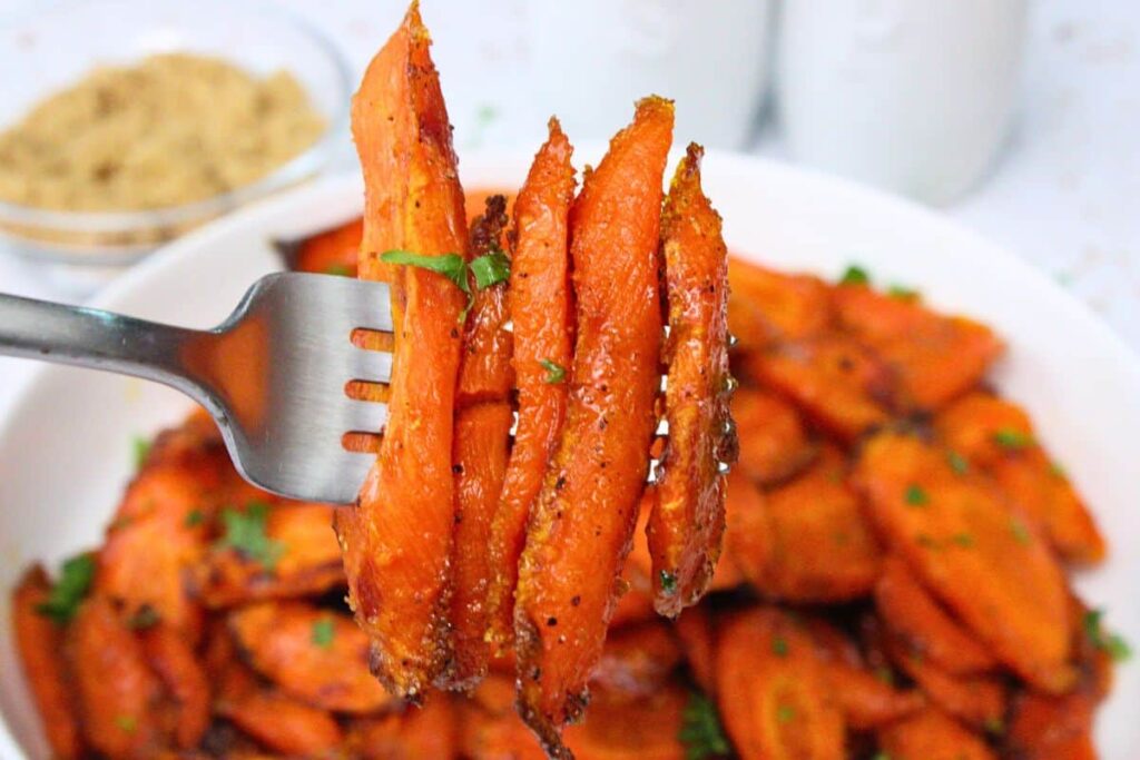 holding up a fork with slices of roasted air fryer brown sugar carrots over a bowl of more