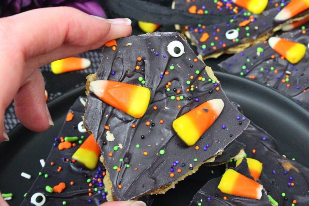 holding up a piece of halloween crack showing off chocolate layer with candy corn, sprinkles, and candy eyes