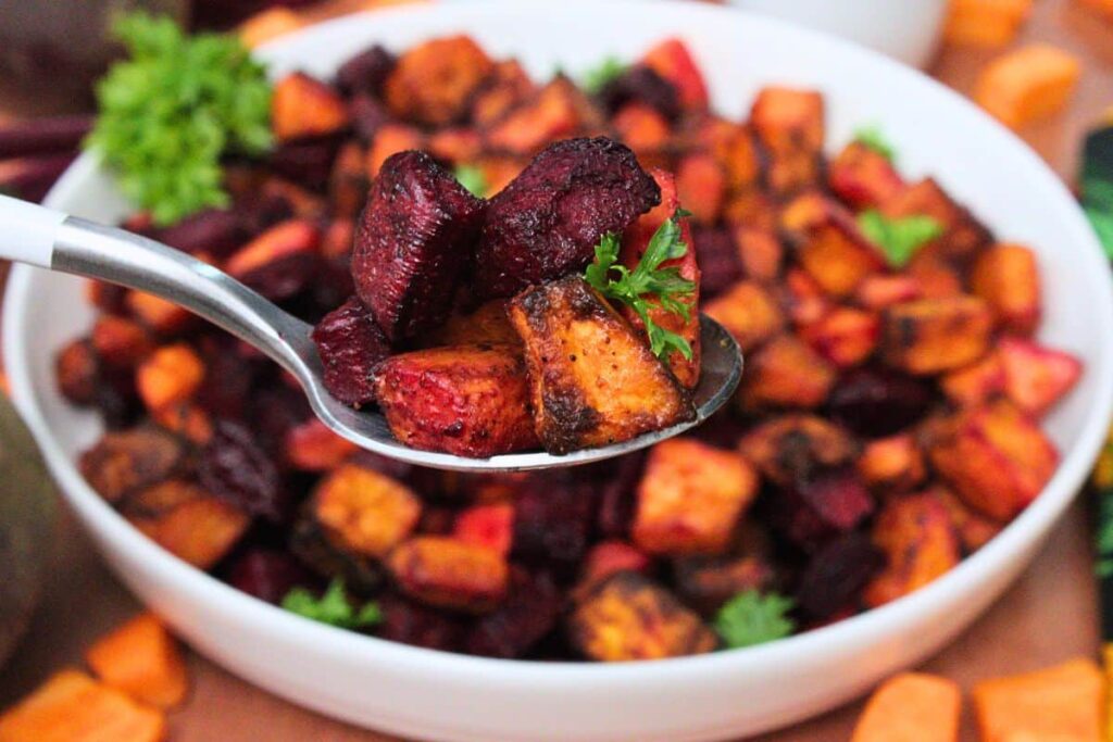 holding up a spoonful of air fryer roasted beets and sweet potatoes over the bowl