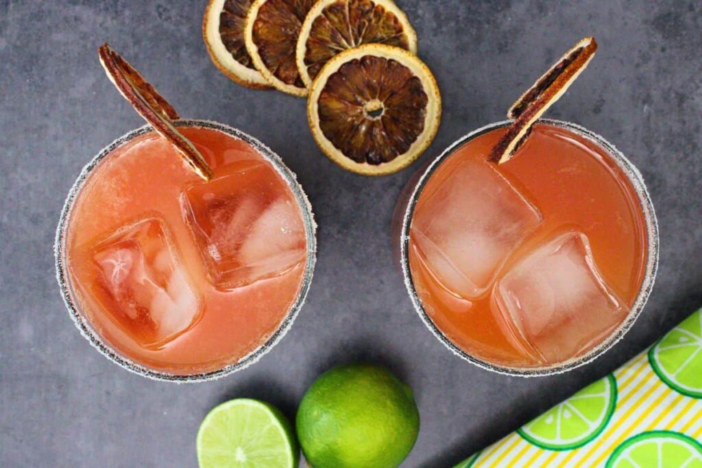 overhead view of two blood orange margarita cocktails with sugar rim and blood orange slice on dark counter
