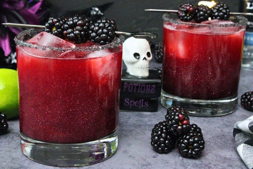 two black magic margaritas with shimmering luster dust with halloween skull decoration in between