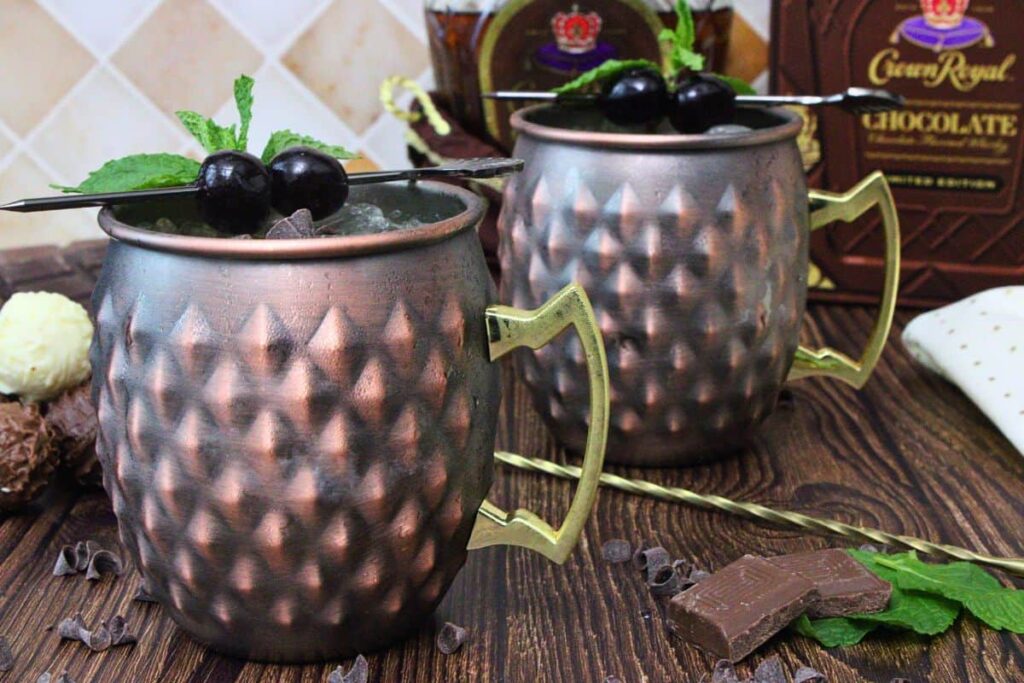 two chocolate mules in copper mugs with cherry garnish surrounded by chocolate pieces