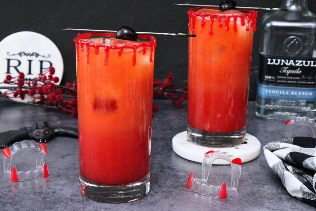 two vampire tequila sunrise cocktails with blood drip rim on a dark background with vampire teeth and bat decorations