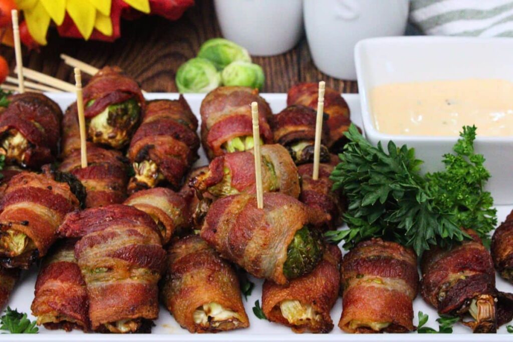 air fryer bacon wrapped brussel sprouts spread across serving platter with side of hot honey ranch sauce