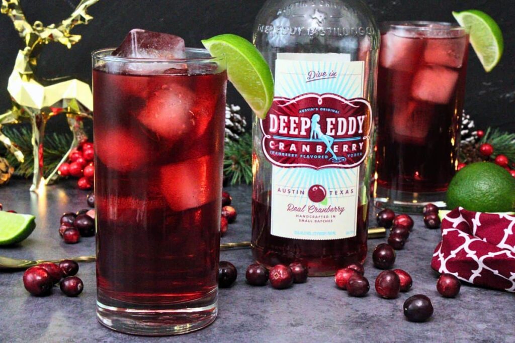 cape codder cocktail with lime next to cranberry vodka bottle amidst elegant holiday decor