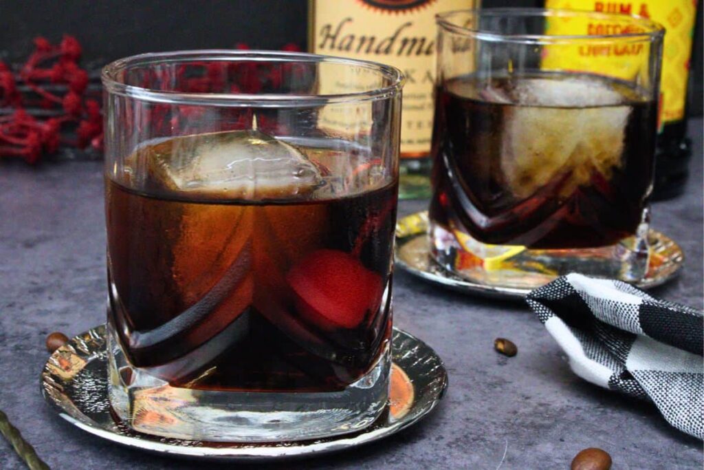 closeup view of two black russian cocktails with a cherry in lowball glasses on a dark counter
