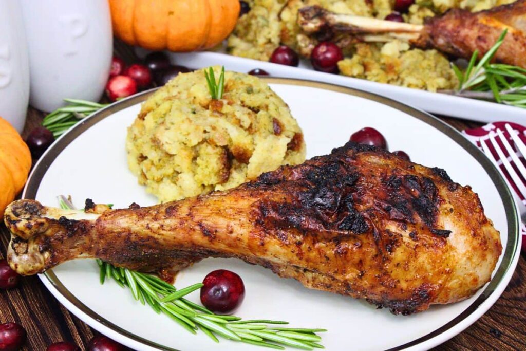 juicy and crispy air fryer turkey leg on a plate with stuffing, cranberries, and a sprig of rosemary