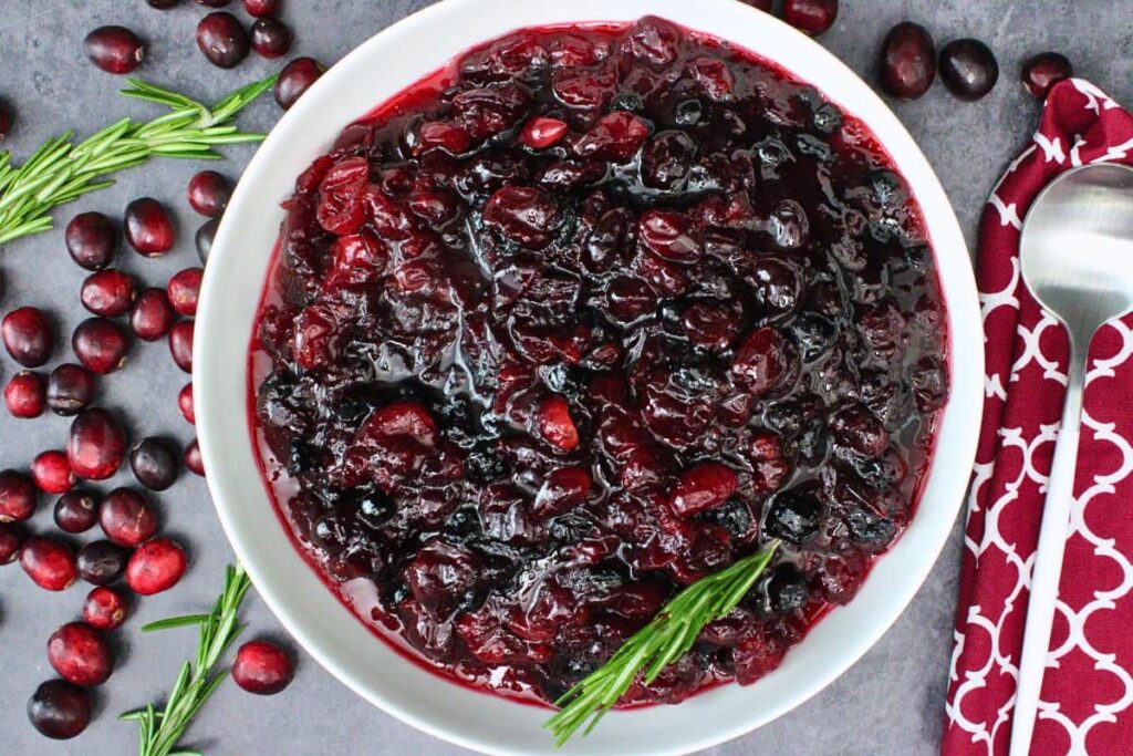 overhead view of microwave cranberry sauce in a white shallow serving bowl with fresh cranberries and rosemary