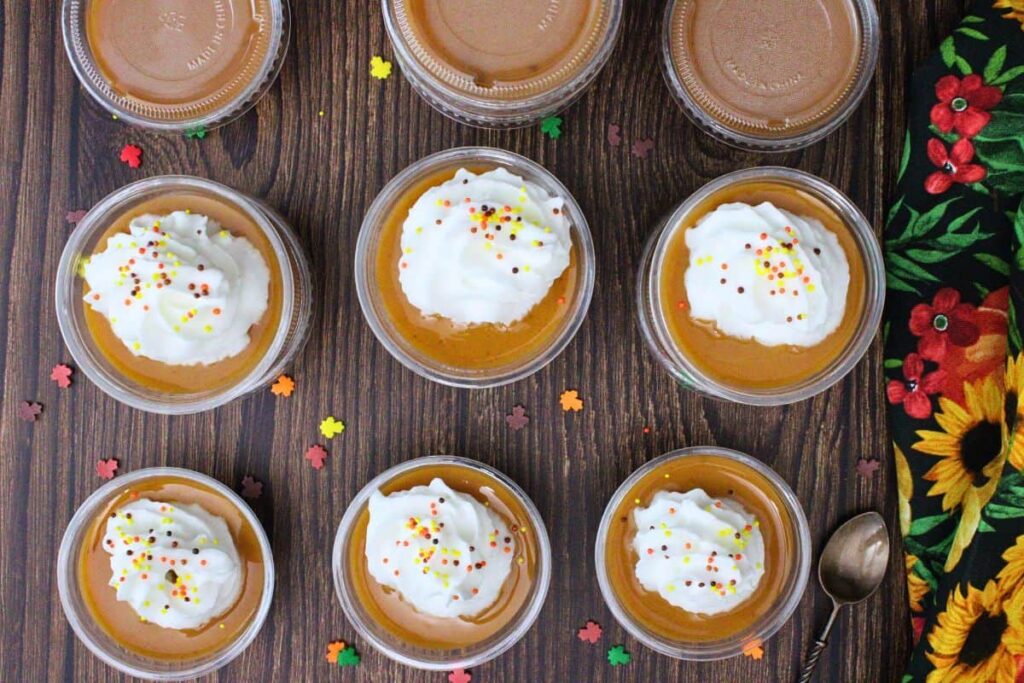 overhead view of pumpkin pie pudding shots with whipped cream and sprinkles on a wooden counter