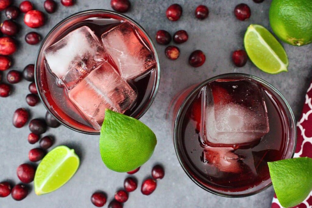overhead view of two cape codder drinks garnished with lime wedge surrounded by fresh cranberries and lime