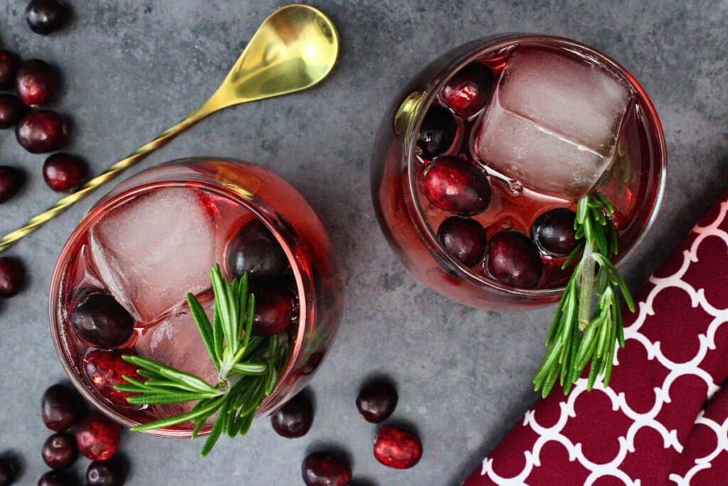 overhead view of two cranberry vodka spritz cocktails with rosemary and cranberry garnish on a dark counter