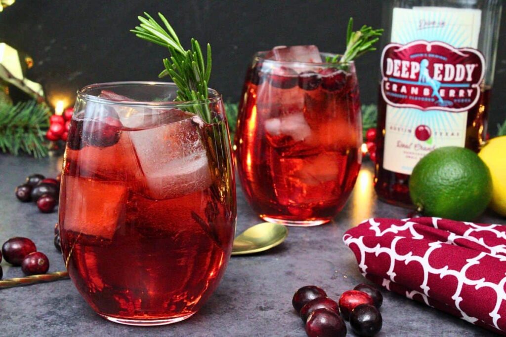 two cranberry vodka spritzer drinks with rosemary garnish and fresh cranberries