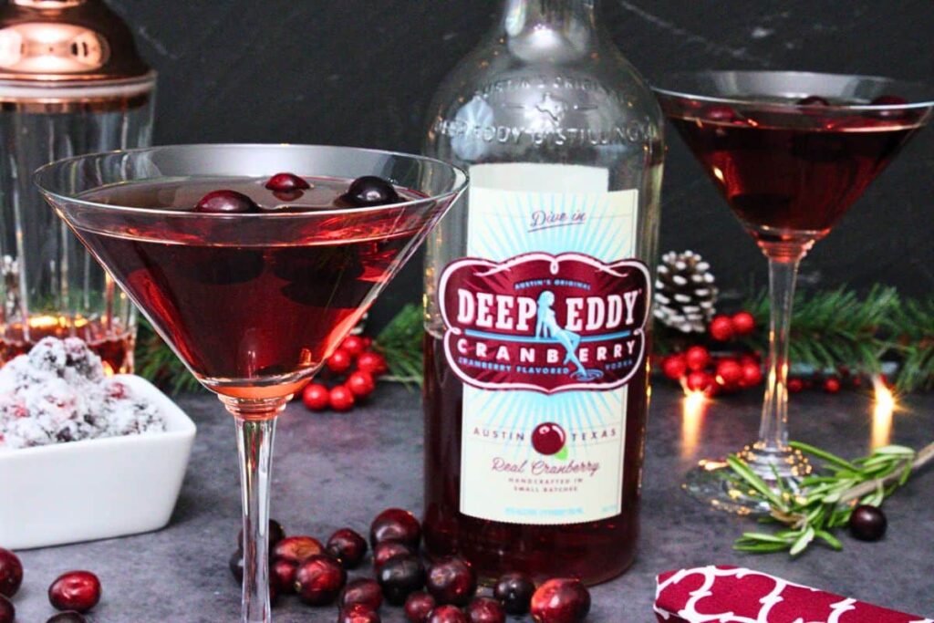 closeup view of cranberry martini with vodka bottle and second martini in the back amidst winter decorations