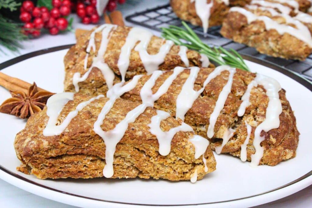 closeup view of three gingerbread scones drizzled with icing glaze on a plate with a sprig of rosemary