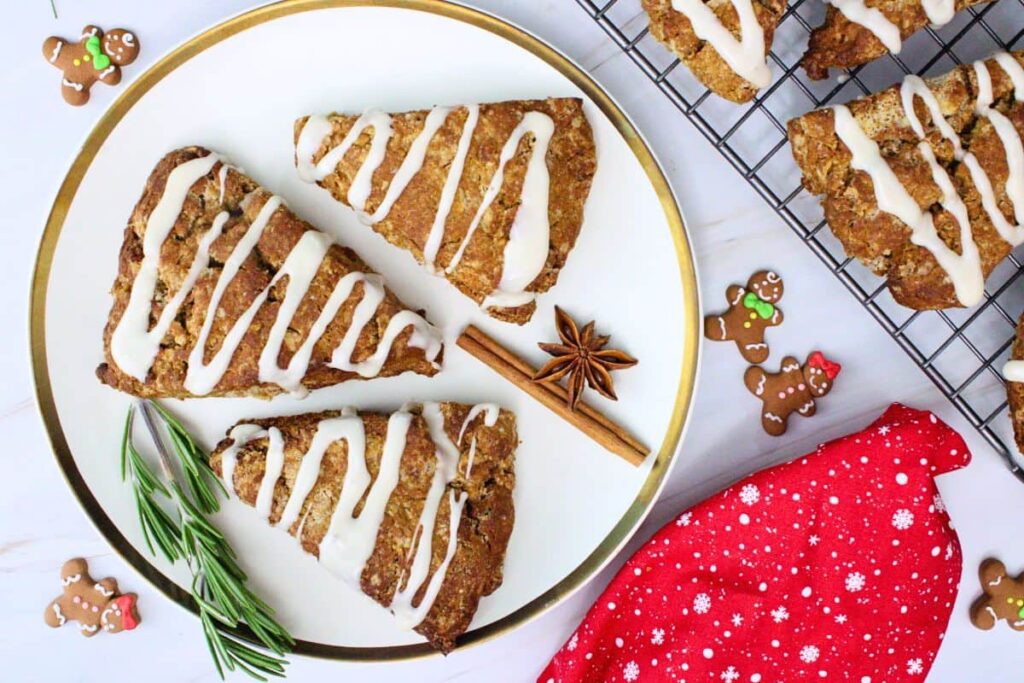 overhead view of three glazed gingerbread scones on a plate with rosemary and small gingerbread cookies for decoration