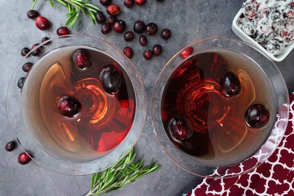 overhead view of two cranberry martini cocktails garnished with fresh cranberries on a dark counter