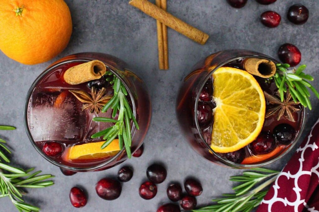 overhead view of two cranberry sangria drinks with fresh cranberries, orange slices, rosemary, star anise, and cinnamon sticks