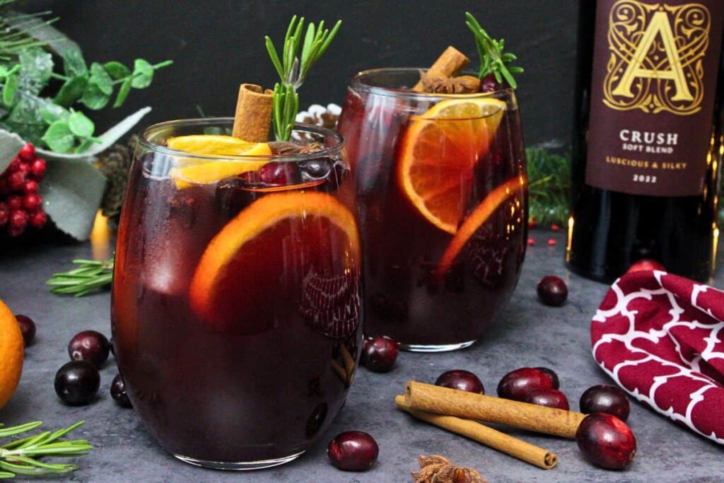 two dark red cranberry sangria drinks garnished with orange and rosemary in front of wine bottle