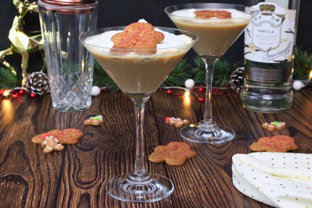 two gingerbread martini drinks with whipped cream and gingerbread man cookie on a wooden counter with more cookies