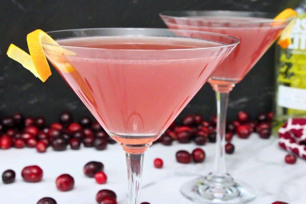 closeup of cosmopolitan cocktail with orange rind twist garnish and additional drink in background