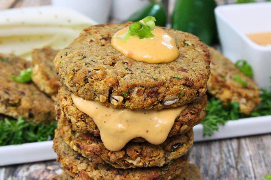 closeup view of black eyed pea fritters stacked in a column with remoulade sauce on top and dripping down the side
