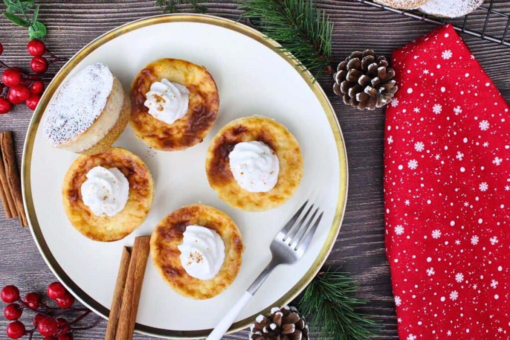 overhead view of four mini eggnog cheesecakes on a plate topped with whipped cream next to a red holiday napkin