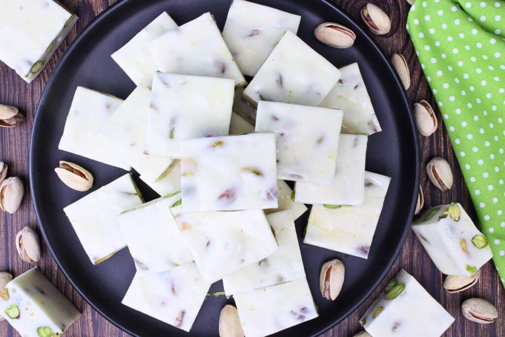 overhead view of pistachio nougat squares on a black plate sitting on a wooden table