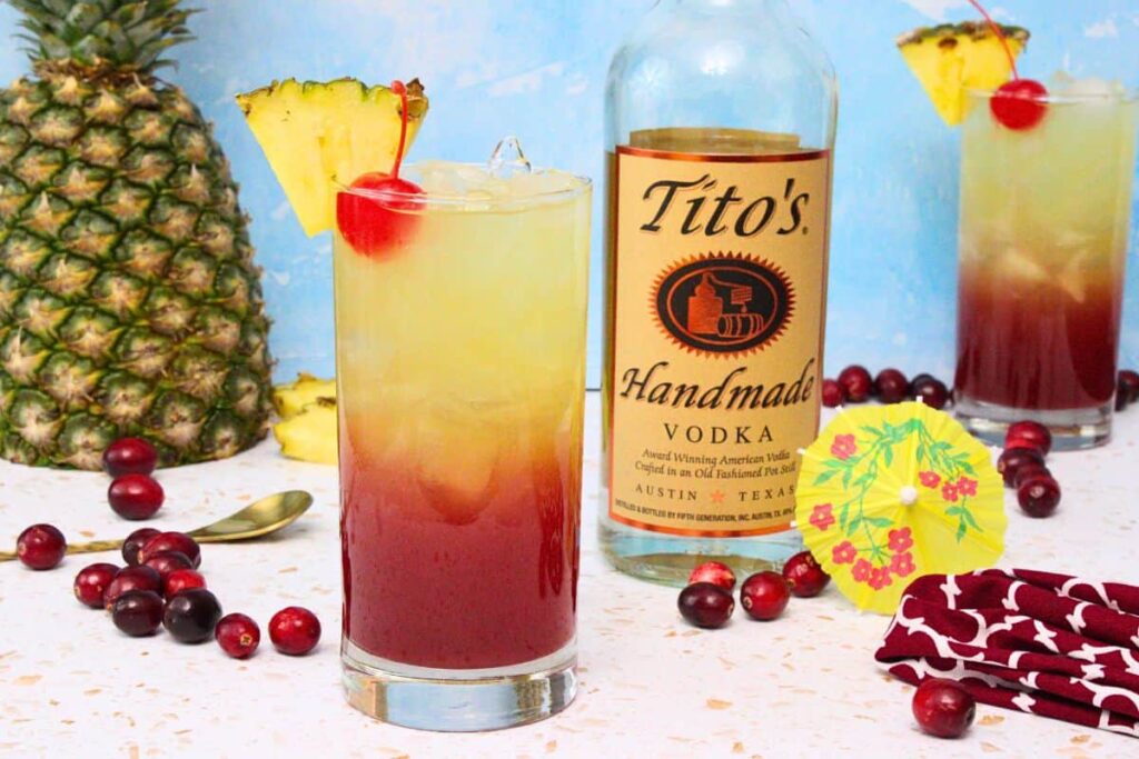 tropical bay breeze garnished with pineapple wedge and cherry next to vodka bottle