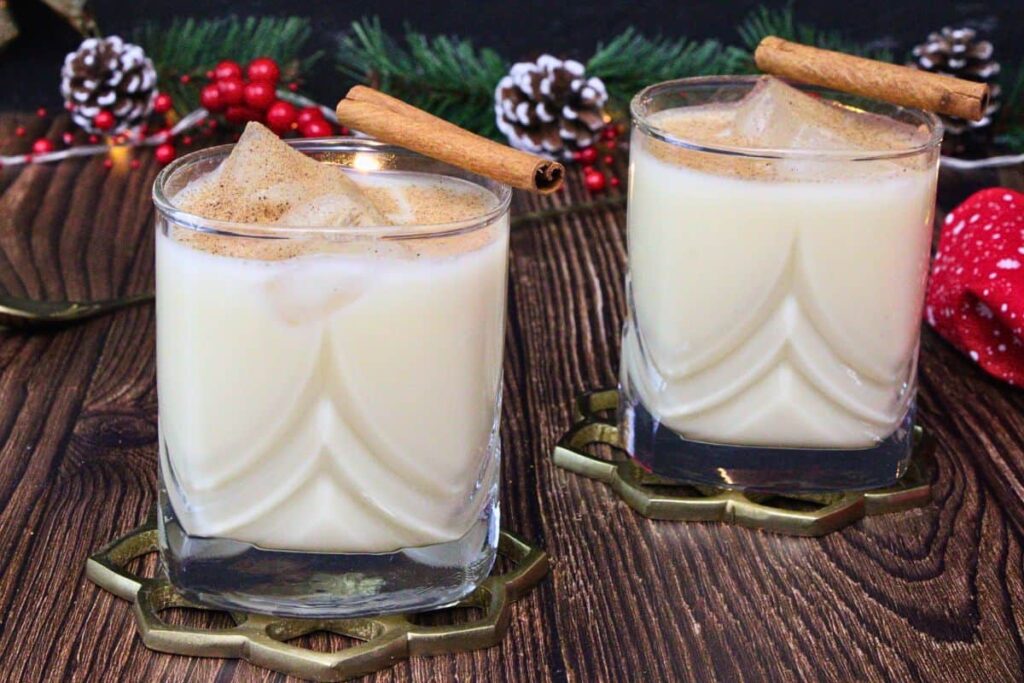 two amaretto eggnog drinks dusted with nutmeg and a cinnamon stick surrounded by winter decor