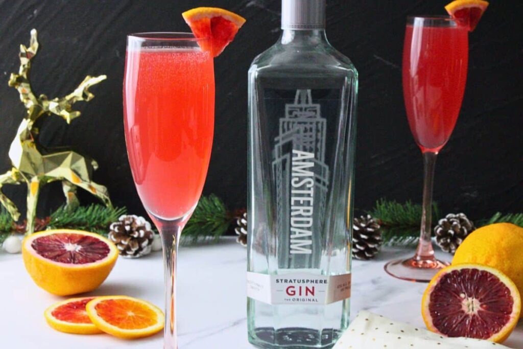 blood orange french 75 in champagne flute with blood orange garnish next to gin bottle