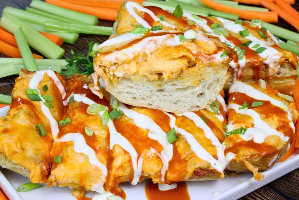 buffalo chicken garlic bread on a serving platter with an extra piece on top drizzled with ranch and buffalo sauce