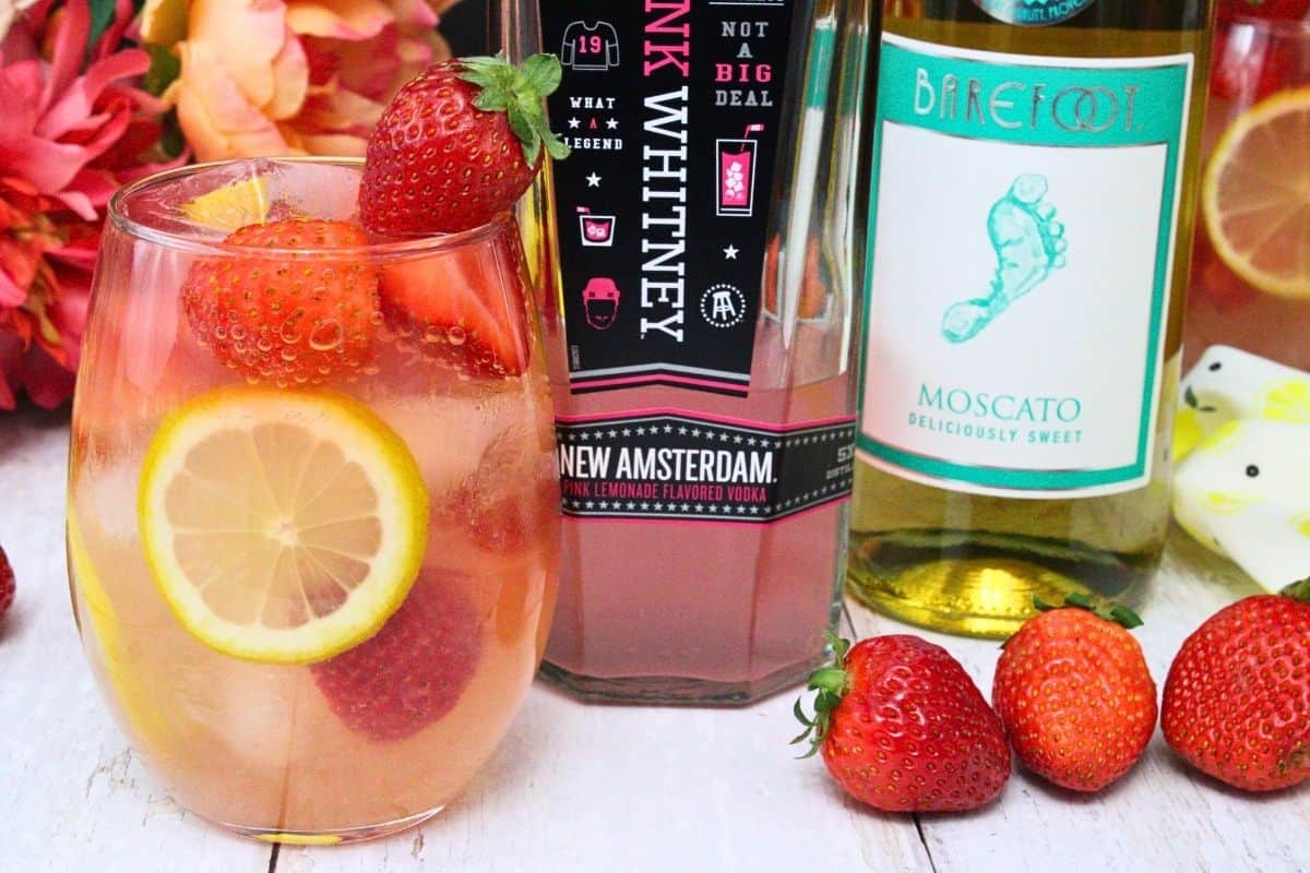 giggle juice cocktail with fresh strawberries and lemon next to alcohol bottles