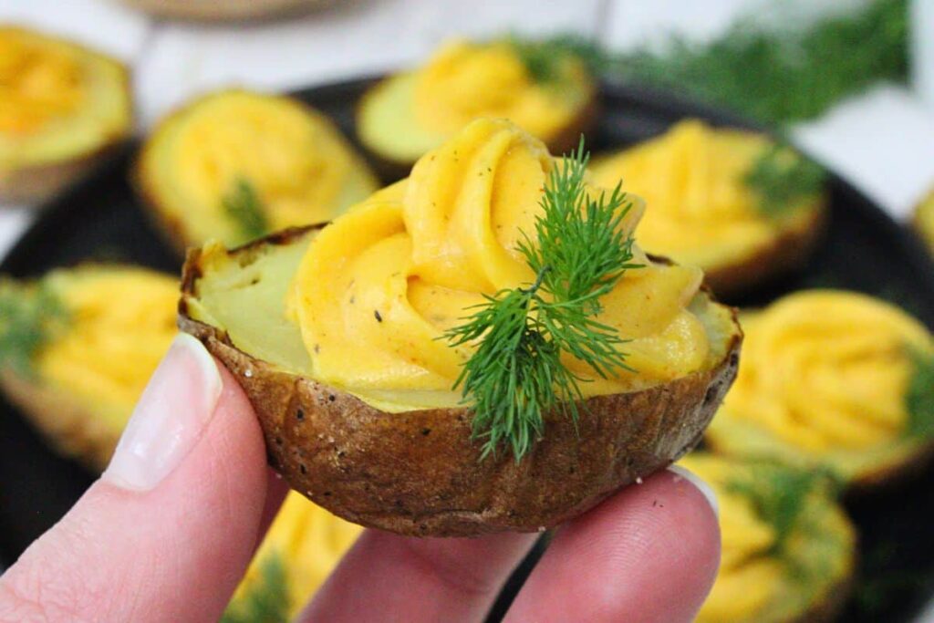 holding up a deviled potato with a sprig of dill on top