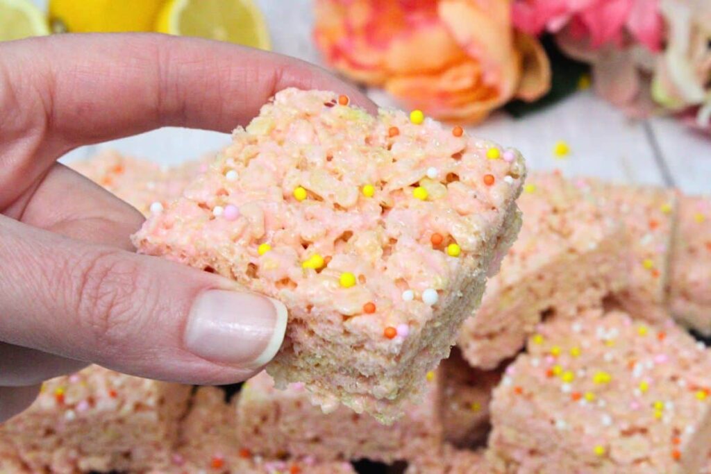 holding up a pink lemonade rice krispie treat showing gooey marshmallows and sprinkle topping