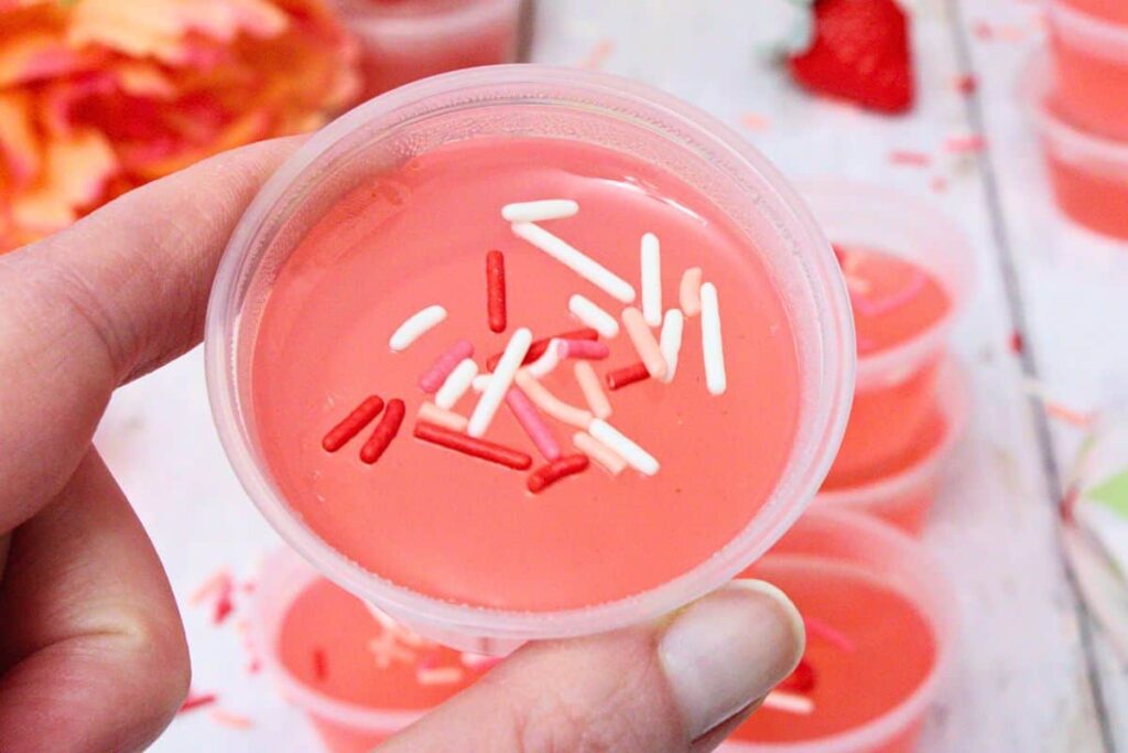 holding up a pink whitney jello shot showing off red, white, and pink sprinkles