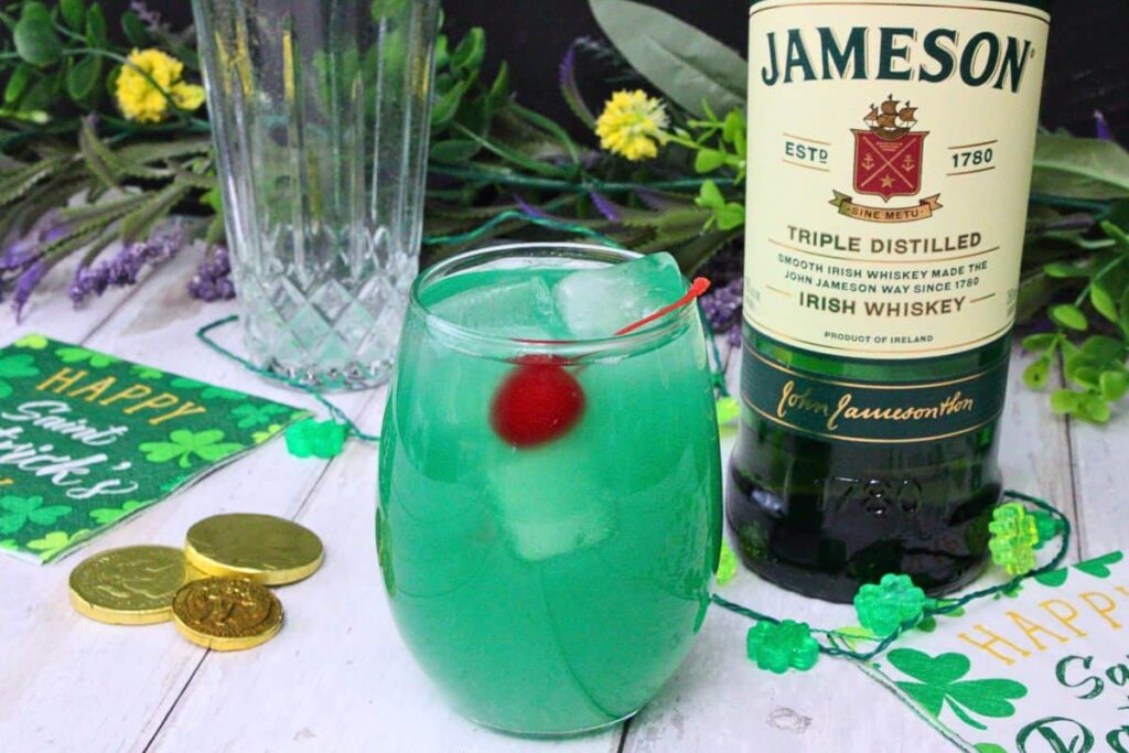 luck of the irish cocktail with cherry in front of whiskey bottle and st patricks day decor