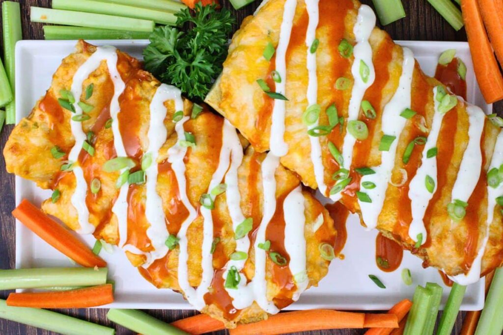 overhead view of french bread buffalo chicken garlic bread drizzled with ranch and buffalo and surrounded by carrots and celery