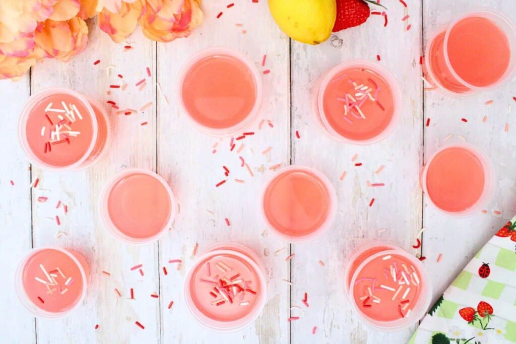 overhead view of pink whitney jello shots topped with sprinkles on a white wooden table