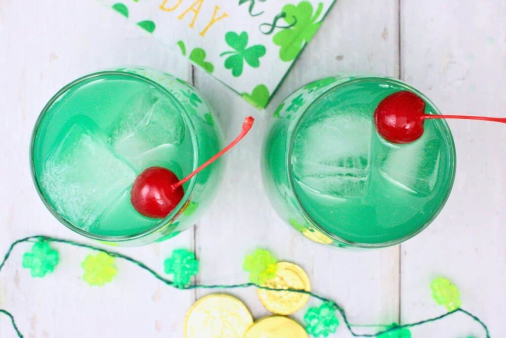 overhead view of two luck of the irish cocktails garnished with cherries on a white wooden table