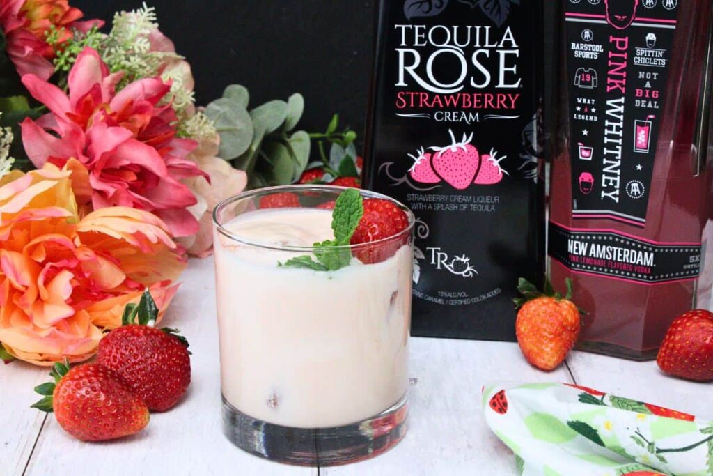 pink russian drink garnished with strawberry and mint in front of liquor bottles